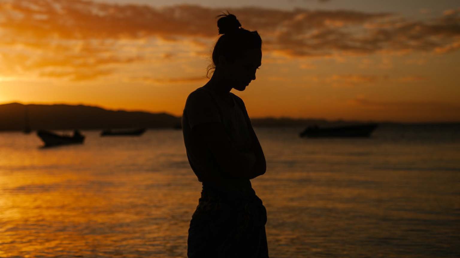 Sad woman standing on coast of sea at sunset